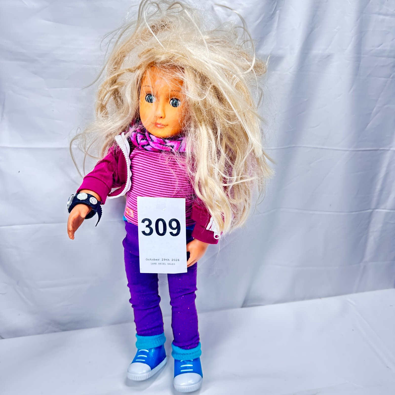 Lot 309: Doll with blonde hair, John Cena WWE championship-style wristwatch accessory, wearing pink top and purple leggings