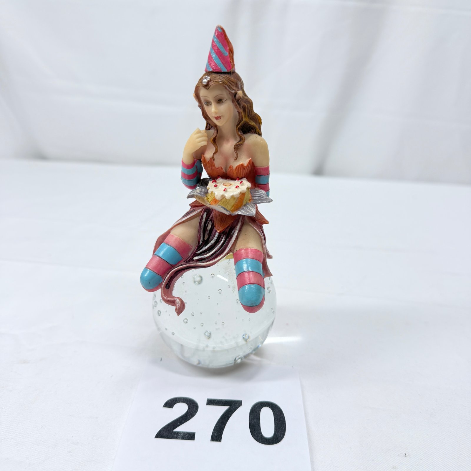 Lot 270: Resin fairy figurine with birthday cake and party hat, seated on glass bubble ball base