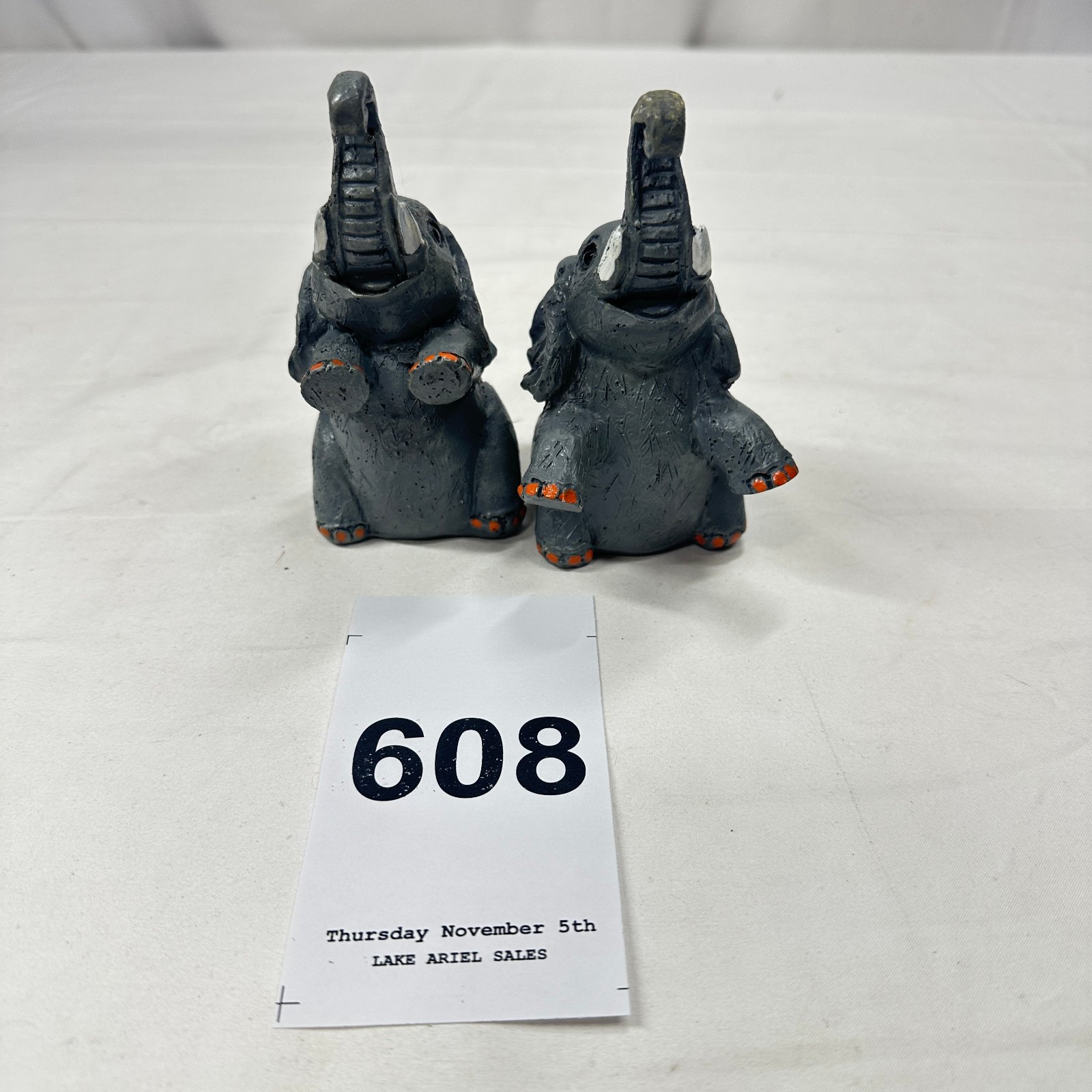 Lot 608: Pair of baby elephant figurines, trunk-up design with orange-painted toenails