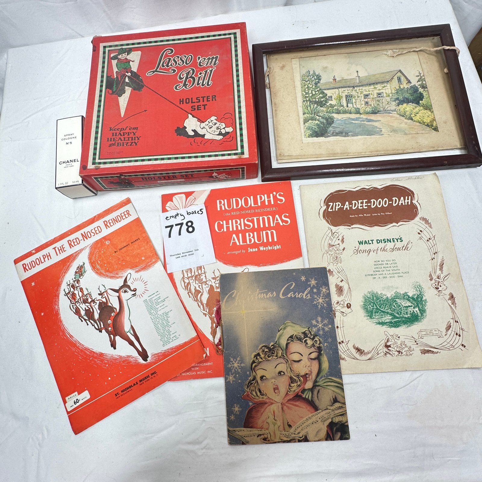 Lot 778: Mixed lot: "Lasso 'em Bill" holster set box, Chanel No.5 cologne box, framed cottage watercolor, Rudolph & Song of the South sheet music, Christmas Carols card