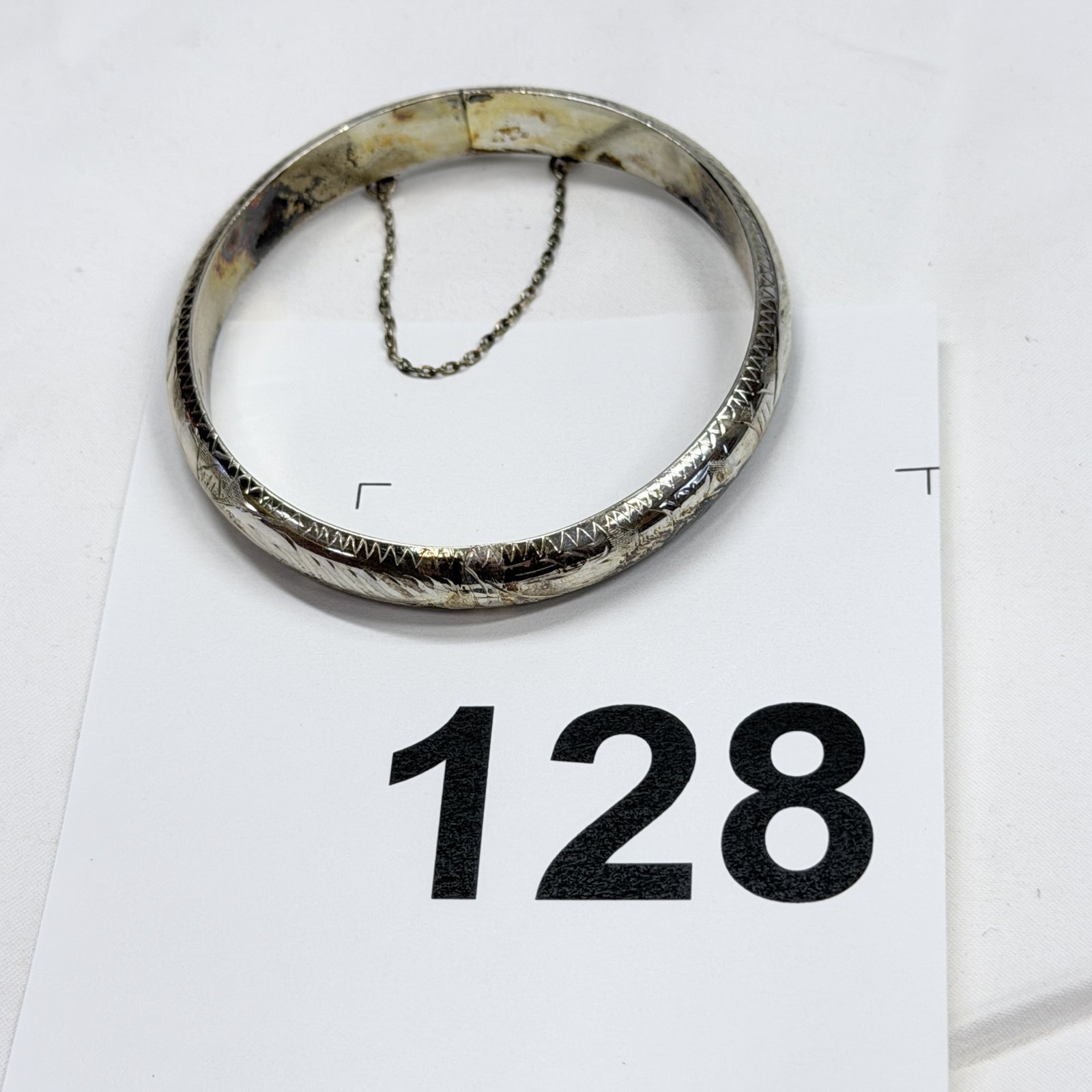 Lot 128: Silver engraved hinged bangle bracelet with safety chain, 13.2g