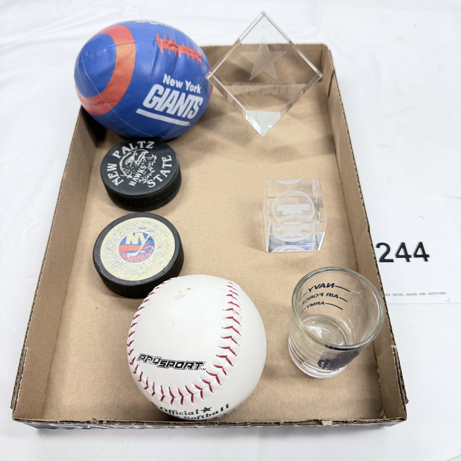Lot 244: Sports memorabilia lot: NY Giants mini football, NY Islanders & New Paltz Hawks pucks, Cowboys/Yankees etched crystal, PROSPORT softball, NAVY/ARMY/AIR FORCE shot glass