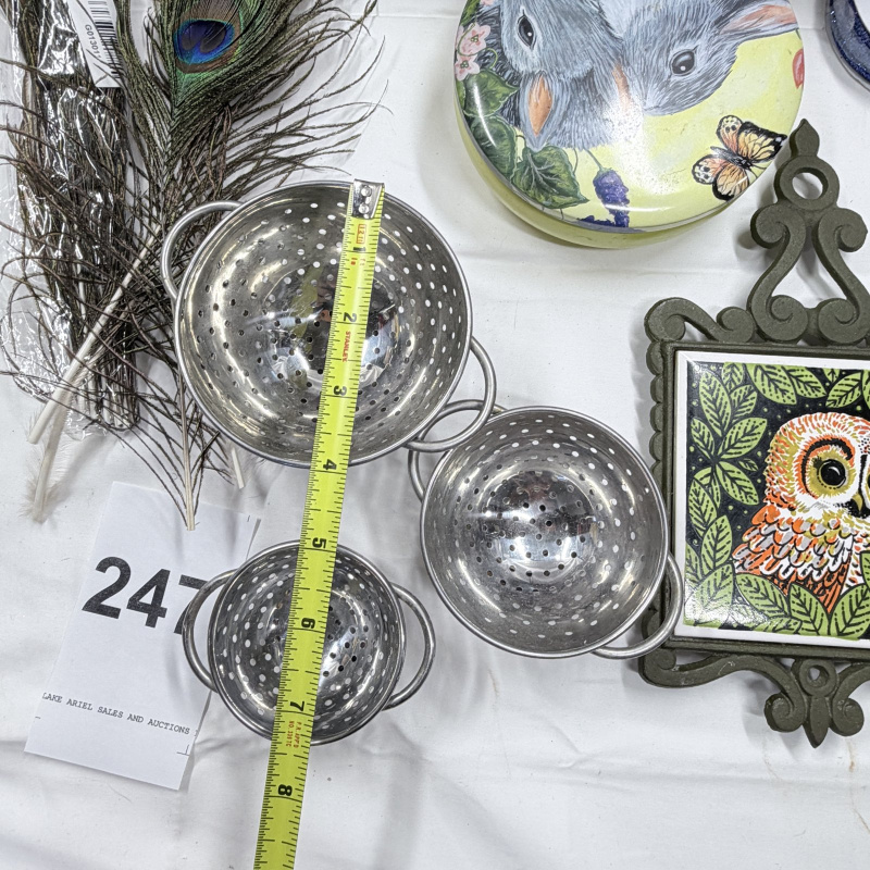 Lot 247: Wicker Basket, Peacock Feathers, Metal Colanders, Owl Decor Plates & Trivet Lot