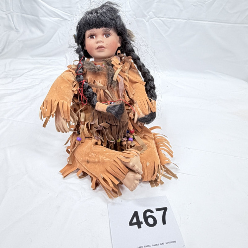 Lot 467: Porcelain Native American girl doll with fringed leather-style dress and braided hair, seated collector's doll